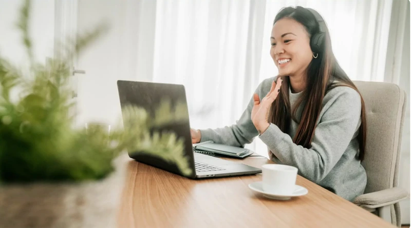 Happy woman working from home with headphones and laptop in a bright, comfortable space